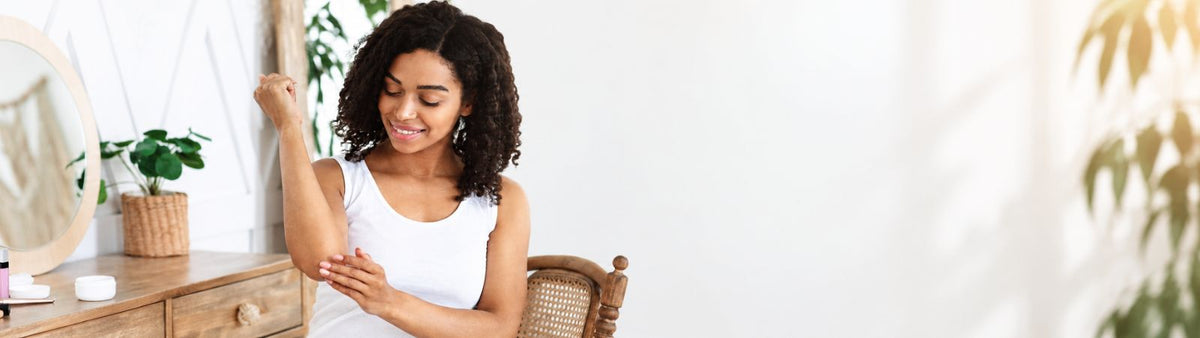 Woman gently applying skincare cream to her inner forearm beside a dressing table.